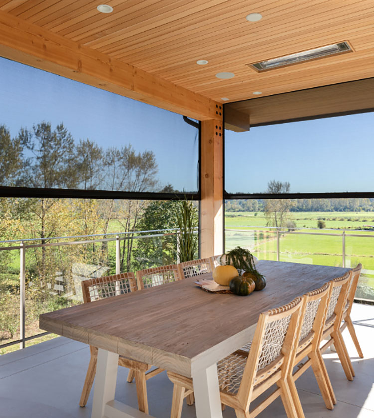 Covered patio with a wooden dining table, wicker chairs, and motorized retractable screens overlooking green fields.
