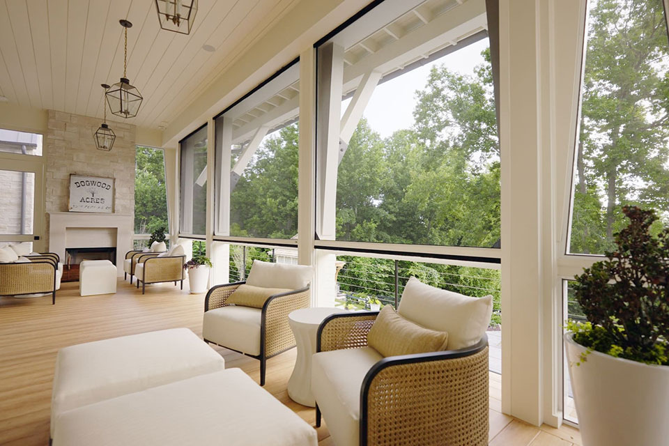 Elegant covered porch with retractable screens, white ceiling, comfortable seating, and panoramic views of surrounding trees and greenery.