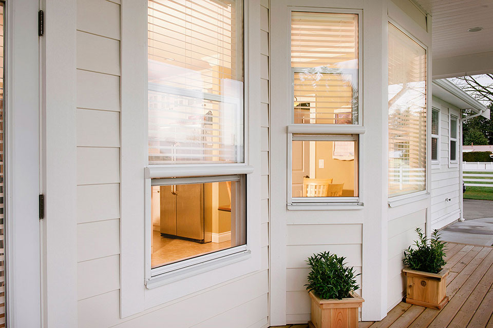 Modern white home exterior with retractable window screens, warm interior lighting, and decorative planter boxes on the porch.