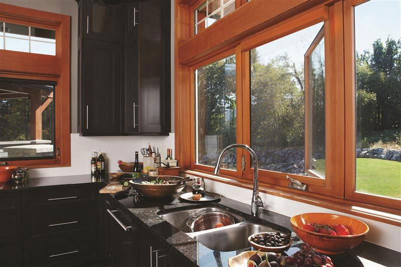 Modern kitchen with wood-framed windows above sink, featuring black granite counters and garden views through unscreened casement windows