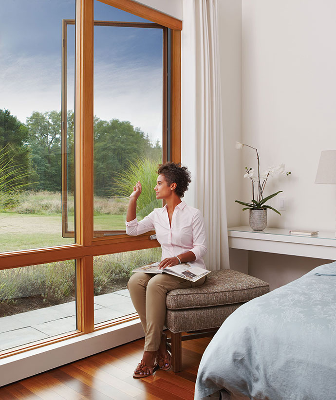 Person reading by a large wood-framed window with natural light streaming in, demonstrating unobstructed views when screen is retracted