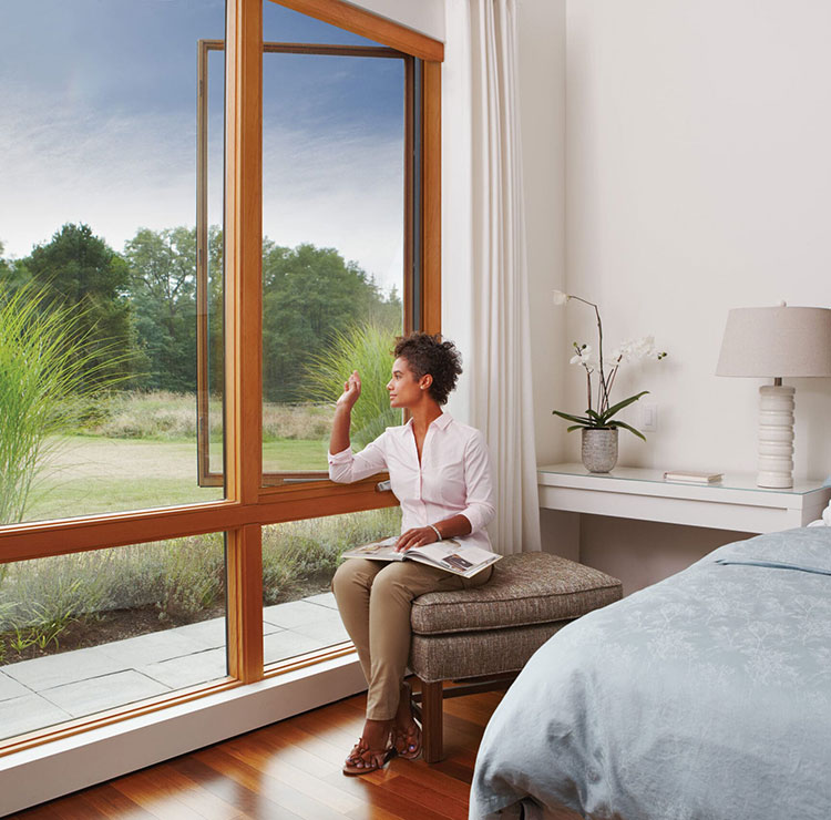 Serene bedroom with wood-framed window overlooking natural grassland, featuring hardwood floors and elegant bedding